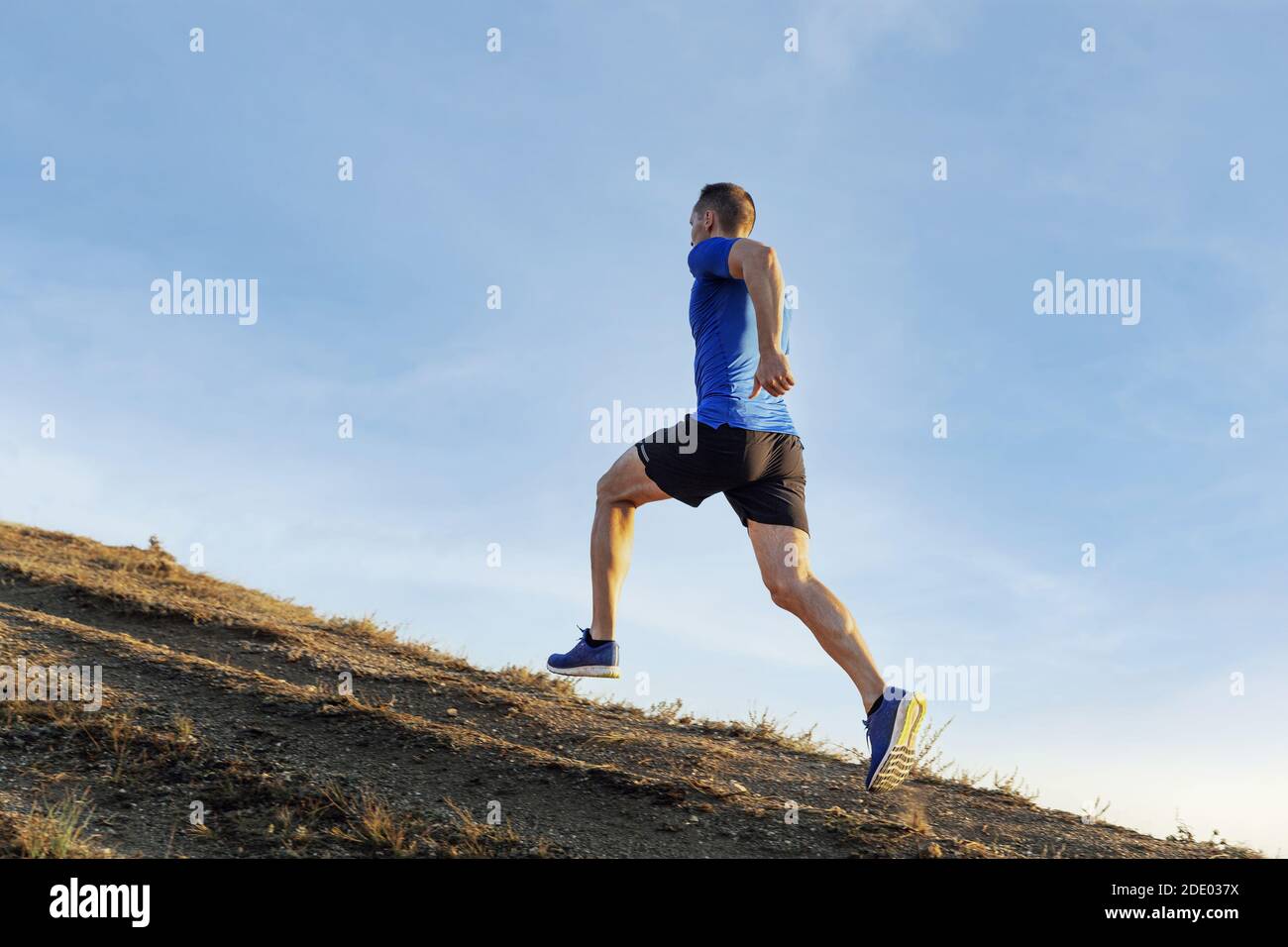 Männlicher Athlet Läufer laufen Bergpfad im Hintergrund Himmel Stockfoto
