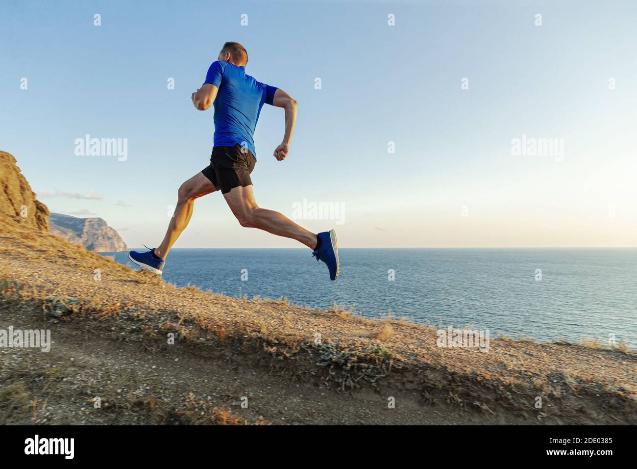 Männlicher Läufer laufen bergauf im Hintergrund Himmel und Meer Stockfoto