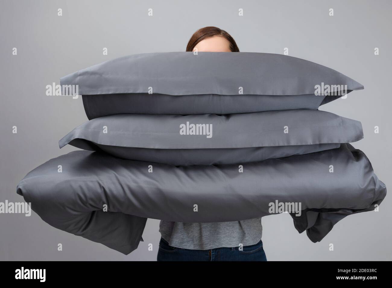 Die Frau hält eine warme Bettdecke und graue Federkissen. Bettwäsche zum Schlafen. Stockfoto