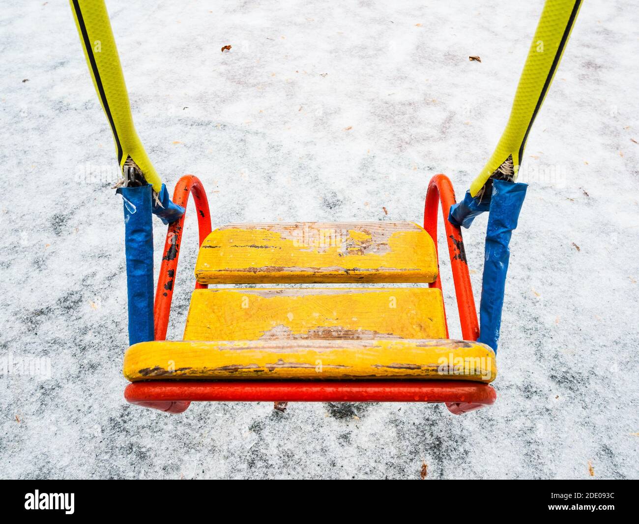 Eisbedeckte gelbe Holzschaukel auf dem Kinderspielplatz nach Glatteisregen am kalten Herbsttag Stockfoto