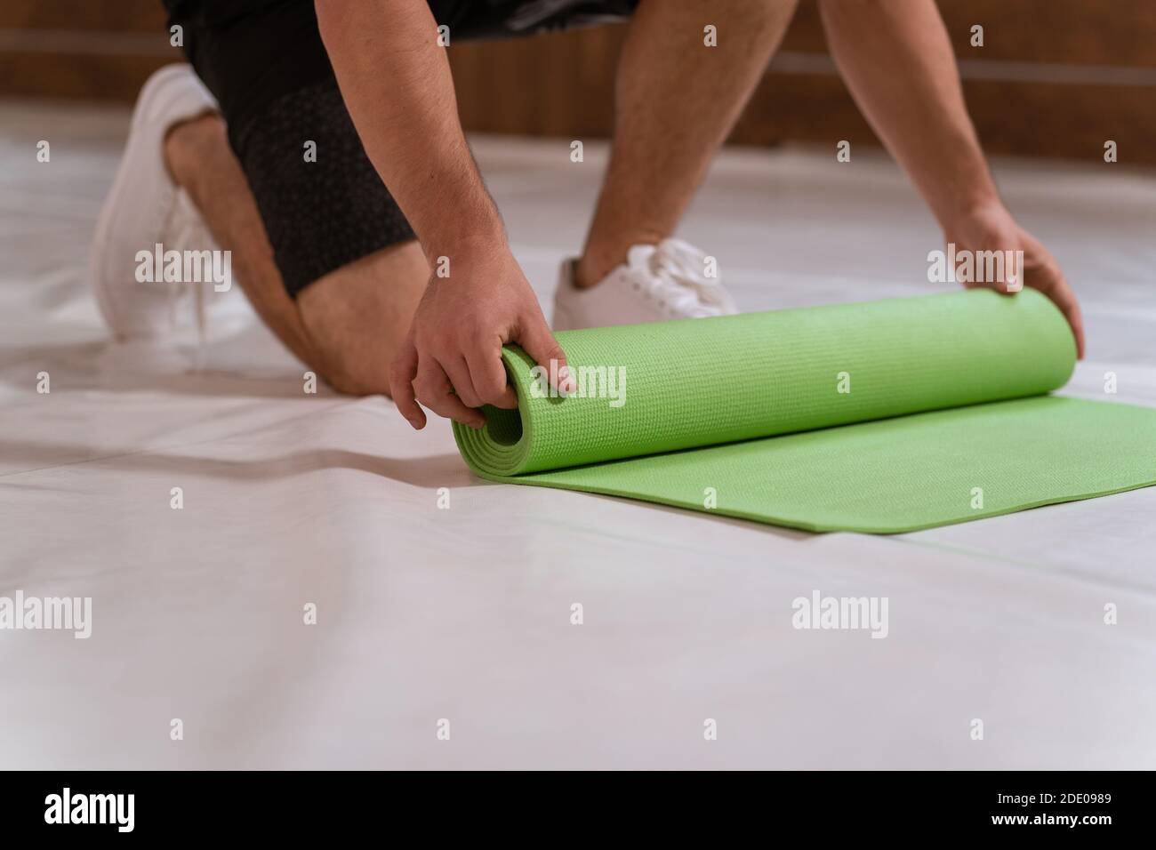Starker, schöner junger Mann, ein Athlet, wickelt eine Rollmatte ab und bereitet einen Platz für den Sport vor. Entschlossener Kerl, der körperliches Training macht Stockfoto