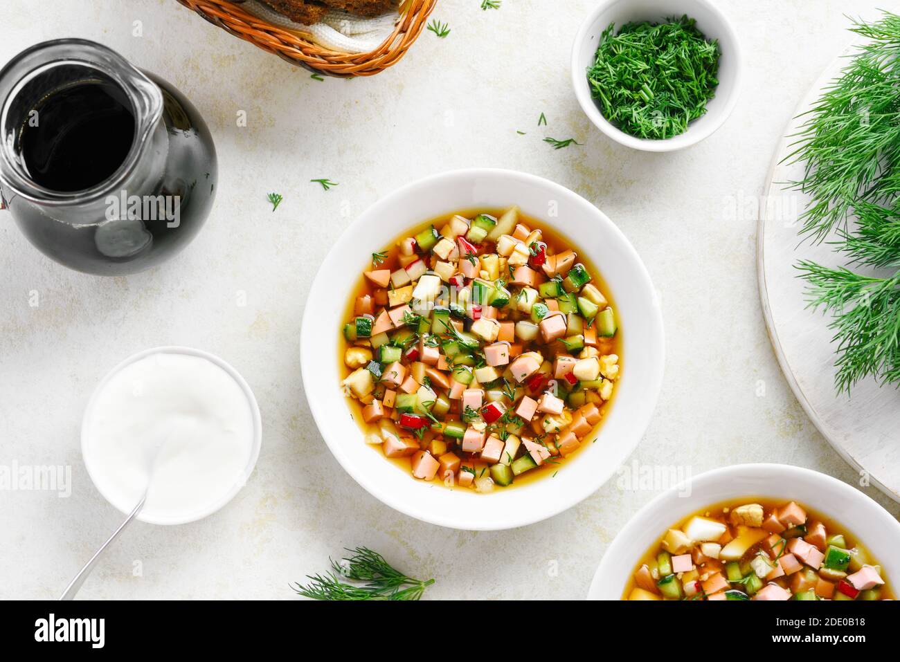 Traditionelle kalte russische Suppe Okroshka mit Wurst, Gemüse und Kvass auf hellem Stein Hintergrund. Draufsicht, flach liegend Stockfoto