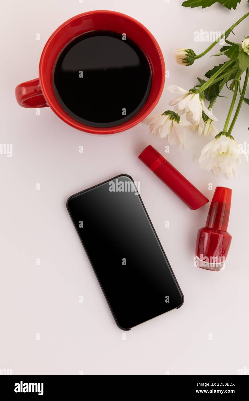 Smartphone, roter Lippenstift, Nagellack, Kaffee und Blumen auf weißem Hintergrund Stockfoto