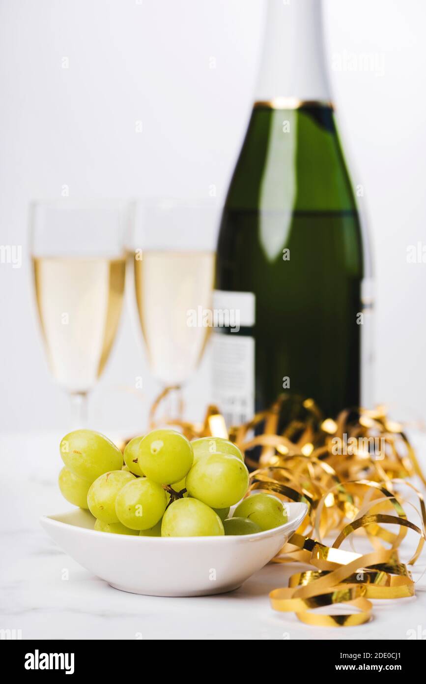 Silvester Feier Konzept Hintergrund. Nahaufnahme der Trauben mit Champagner-Flasche und zwei Gläser verschwommen auf dem Hintergrund auf Marmortisch. Sele Stockfoto
