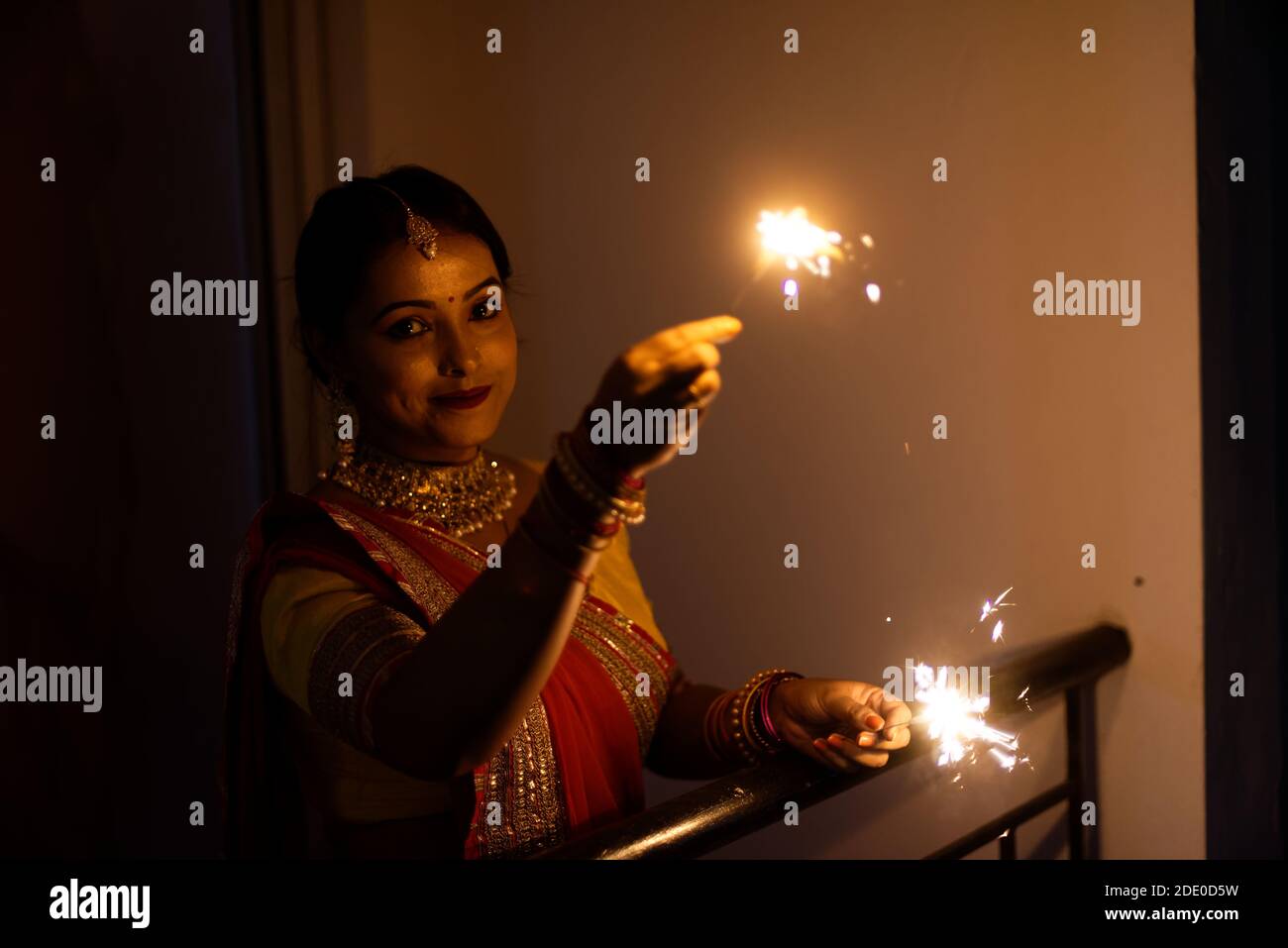 Die junge und schöne indische Bengalin in indischer Tracht feiert Diwali mit Feuercrackern auf einem Balkon in Dunkelheit. Stockfoto