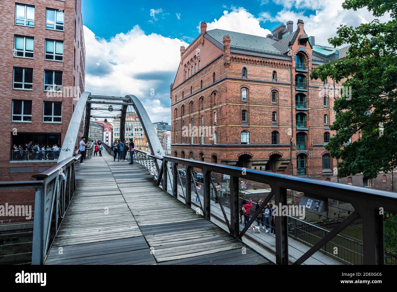 Hamburg, Deutschland - 21. August 2019: Fußgängerbrücke über einen Kanal mit Menschen und einem alten klassischen Lagerhaus in der HafenCity, Hamburg, Deutschland Stockfoto