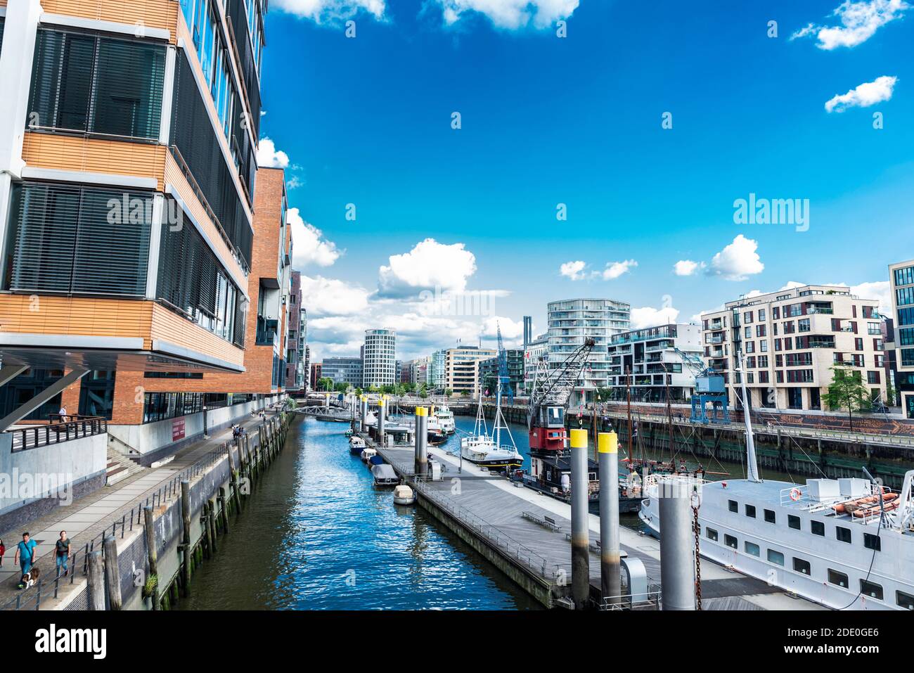 Hamburg, 21. August 2019: Moderne Gebäude und eine Anlegestelle mit Booten und Menschen in der Nähe eines Kanals im Stadtteil HafenCity, Hamburg Stockfoto