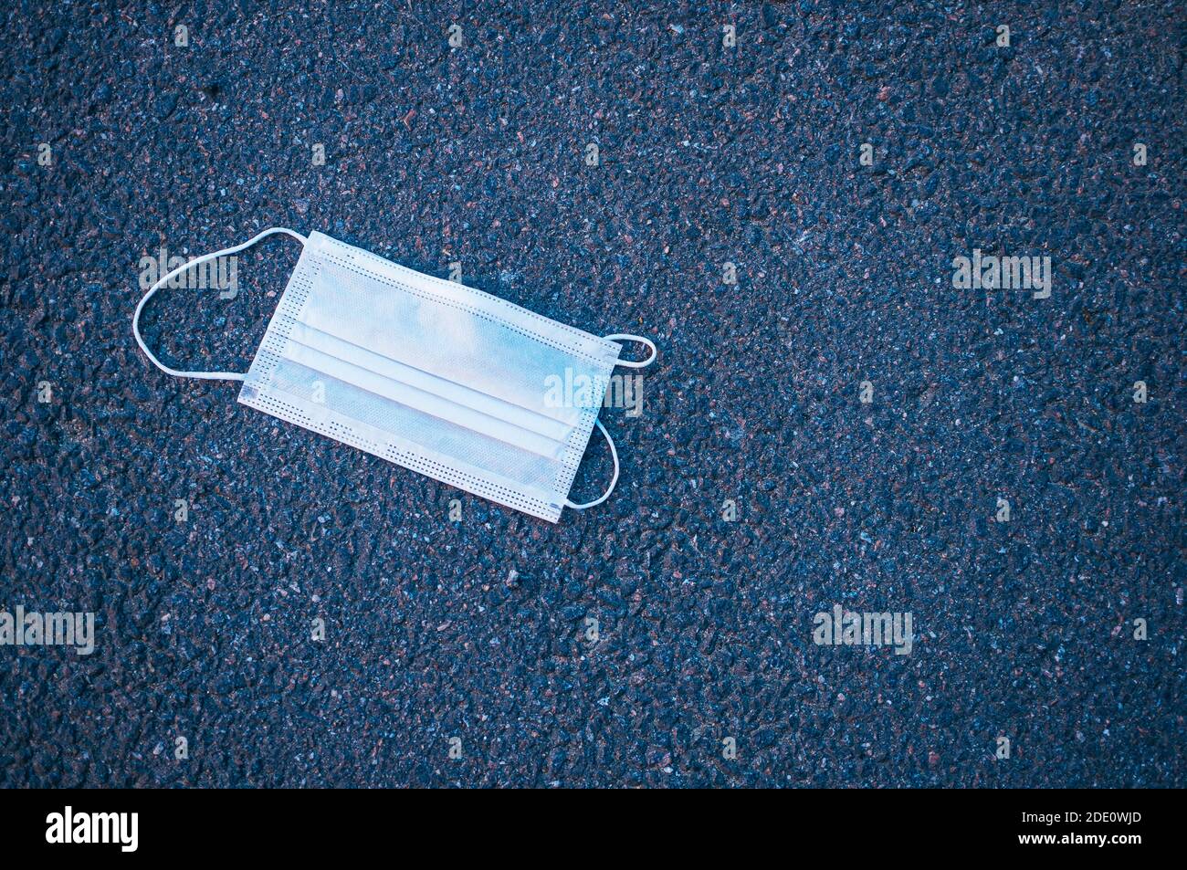 Medizinische Schutzmaske auf dem Asphalt. Epidemische zweite Welle Konzept. Getöntes Foto mit Vignettierung. Draufsicht. Stockfoto