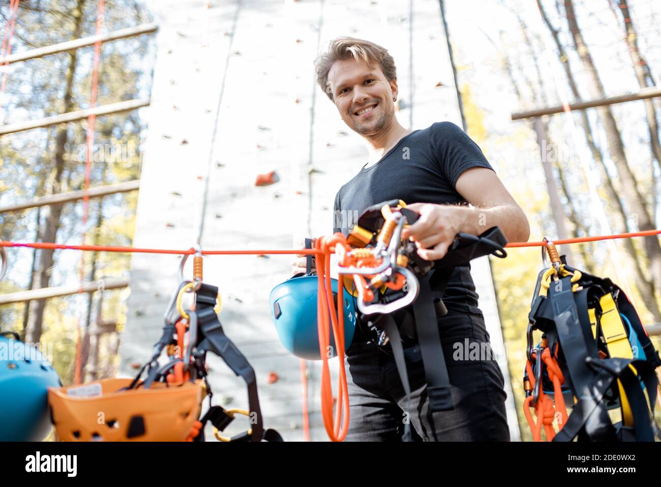 Schöner Mann trägt Sicherheitsausrüstung zum Klettern im Vergnügungspark, Vorbereitung für das Klettern an der Wand Stockfoto