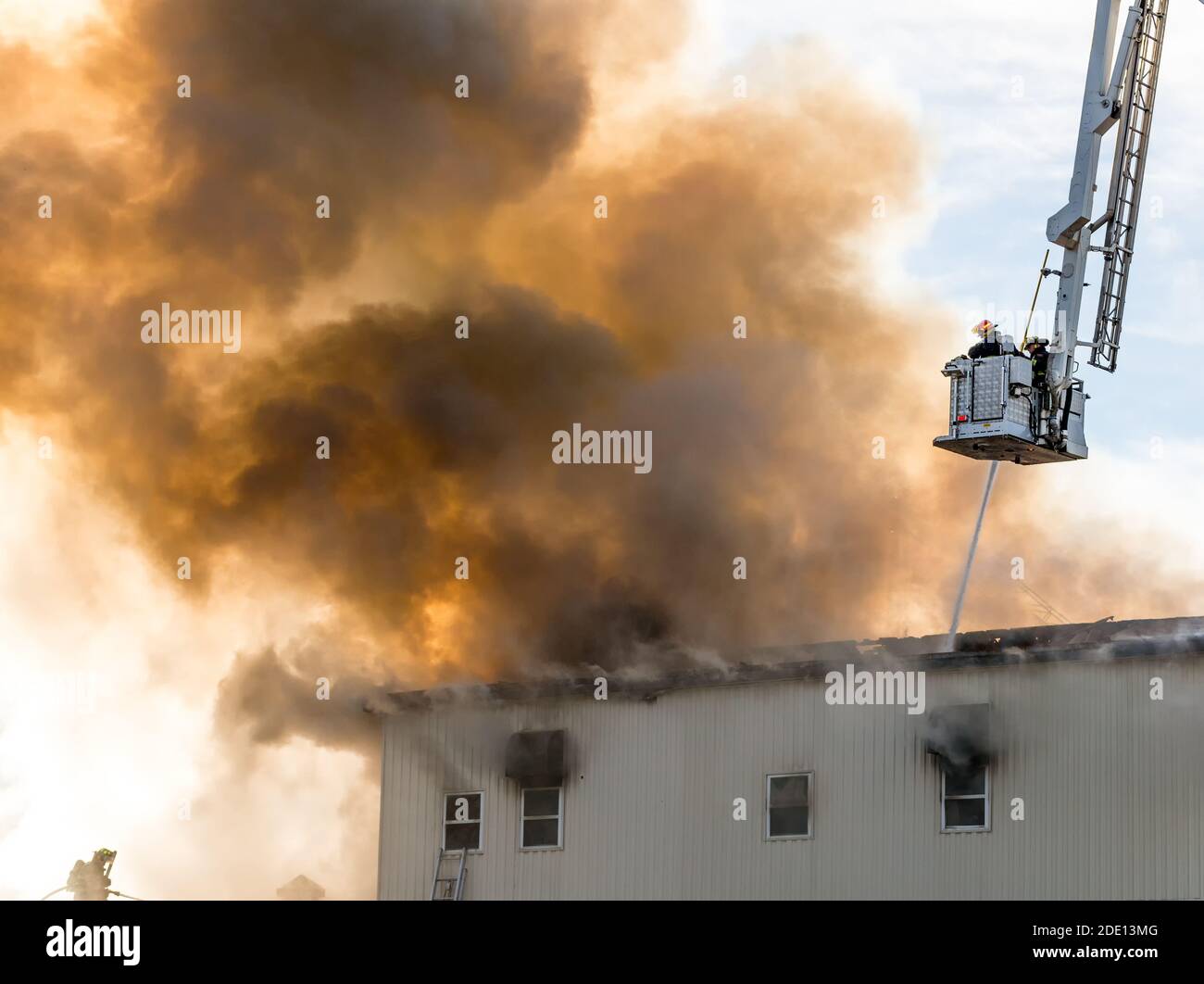 Zwei Feuerwehrmänner bekämpfen das Gebäude Feuer aus Eimer oben. Ein Schlauch sprüht Wasser durch den Rauch. Die Feuerwehrleute tragen Atemgeräte. Stockfoto