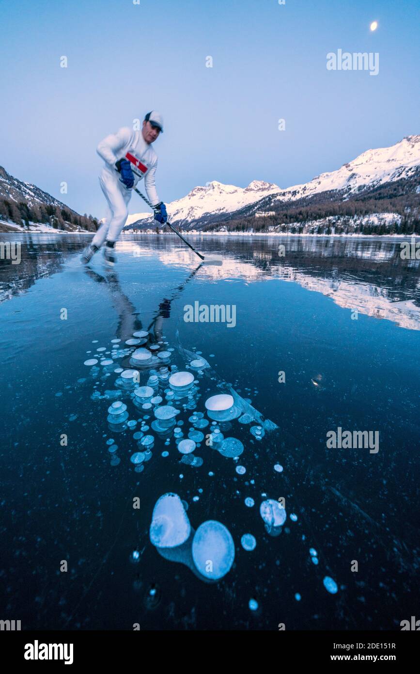 Eishockey-Spieler Mann Skating auf dem Sils in Eisblasen in der Dämmerung bedeckt, Engadin, Graubünden Kanton, Schweiz, Europa Stockfoto