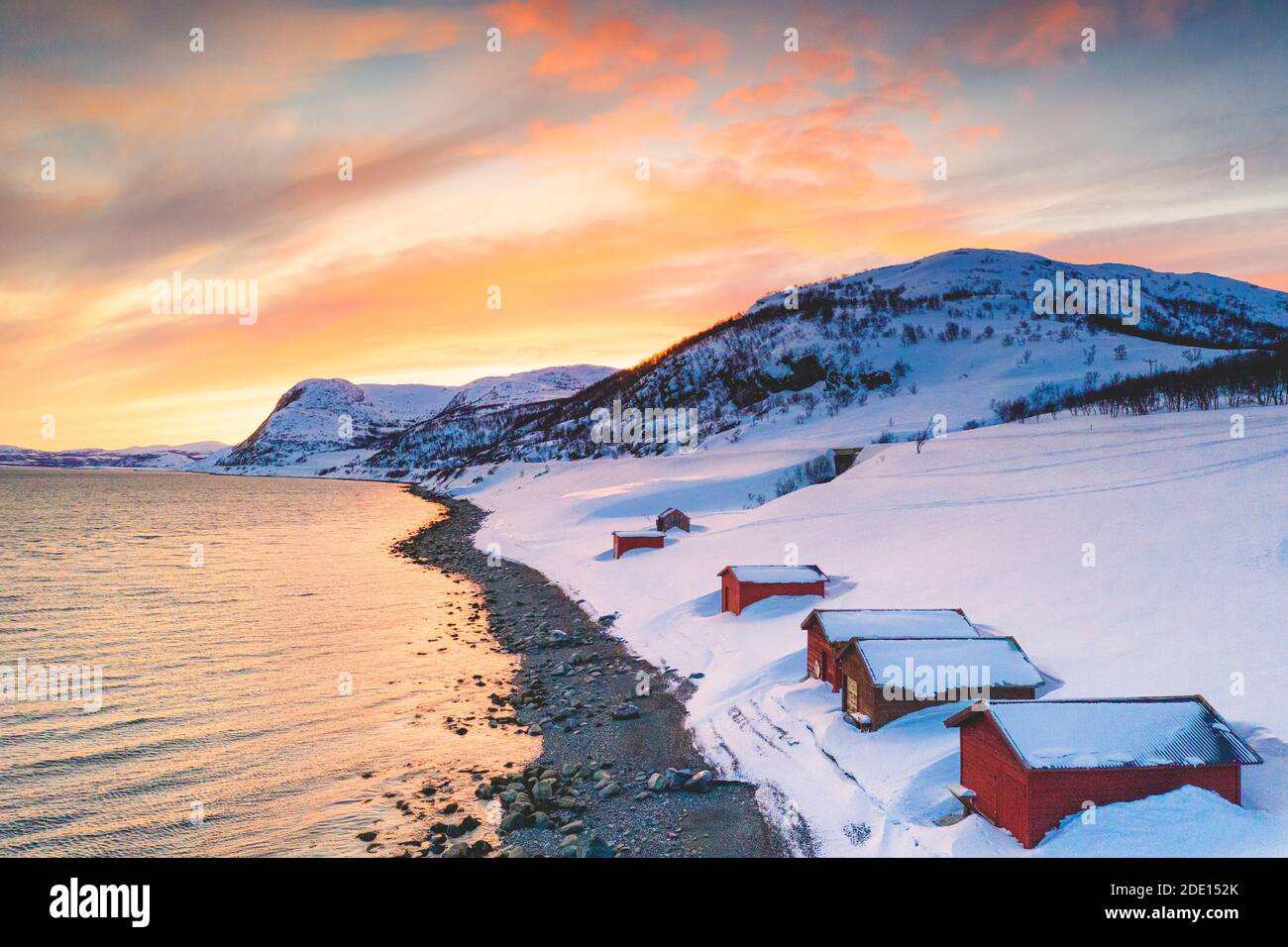 Sonnenuntergang über roten Hütten im Schnee entlang Porsangerfjord mit Nordkap (Nordkapp) im Hintergrund, Troms Og Finnmark, Arktis, Norwegen Stockfoto