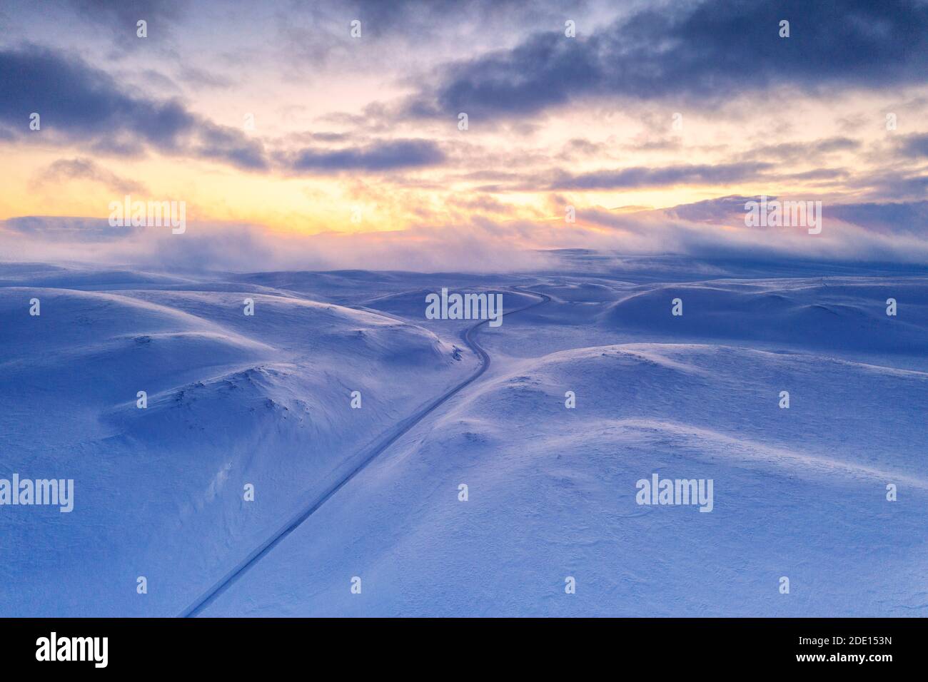 Arktischer Sonnenuntergang über Tanafjordveien leere Straße über die schneebedeckten Berge nach Schneesturm, Tana, Troms Og Finnmark, Arktis, Norwegen Stockfoto