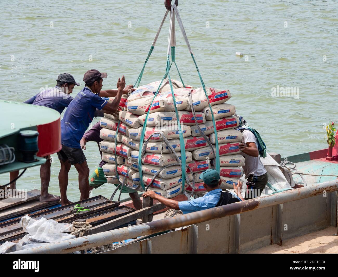 Arbeiter senken Zementsäcke von Siam Cement in einem Slingbag auf ein Boot im Hafen von Myeik, Tanintharyi Region, Myanmar. Stockfoto