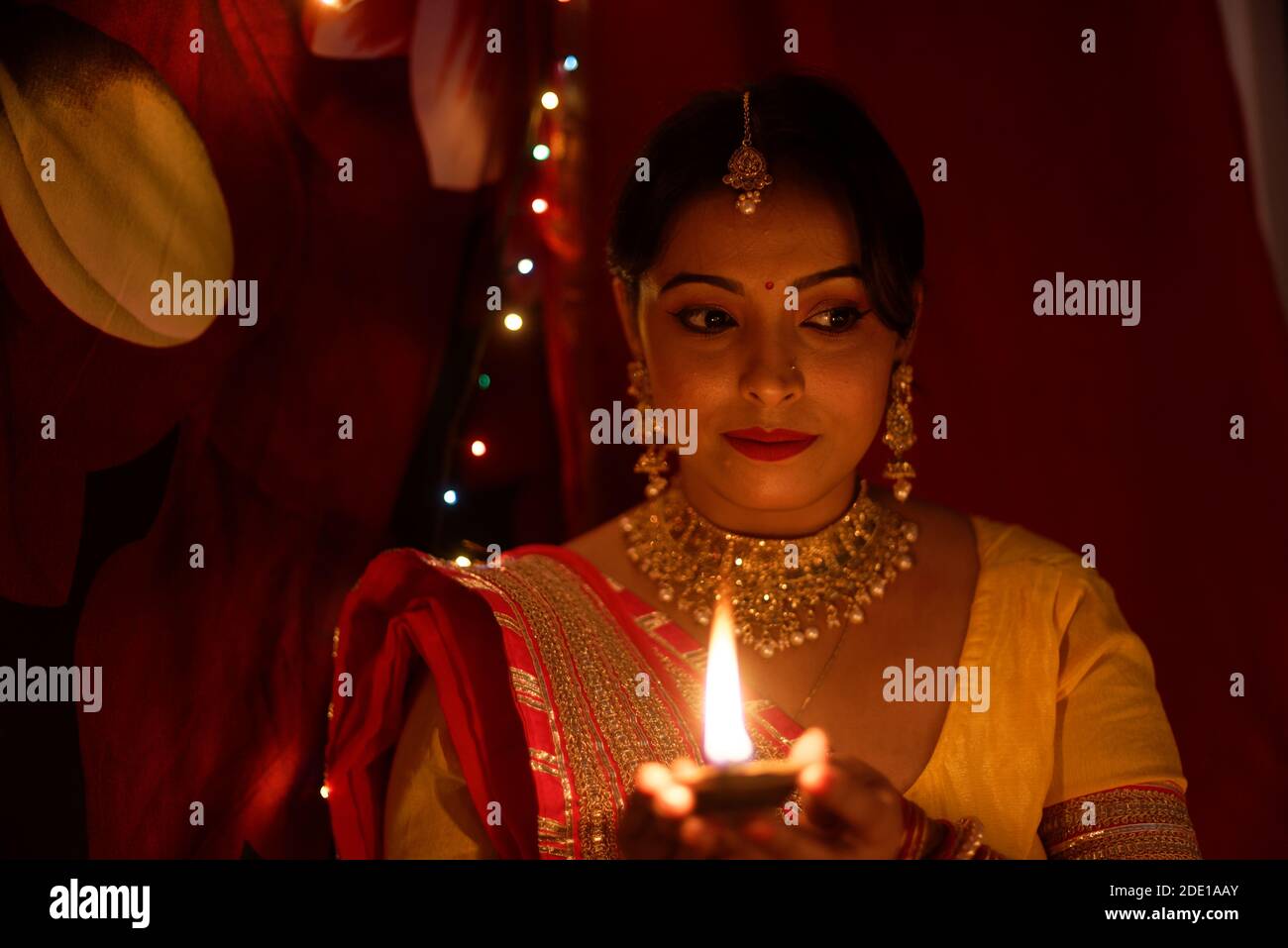 Eine junge und schöne indische Bengalin in indischer Tracht hält eine Diwali diya/Lampe in der Hand vor bunten Bokeh-Lichtern. Stockfoto