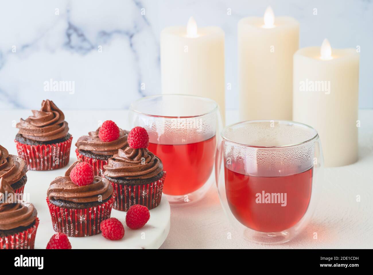 Schokolade Cupcakes mit Schokolade Buttercreme Zuckerguss mit frischen Himbeeren verziert, und Himbeer-Tee in Glas Tassen schließen auf hellem Hintergrund. Stockfoto