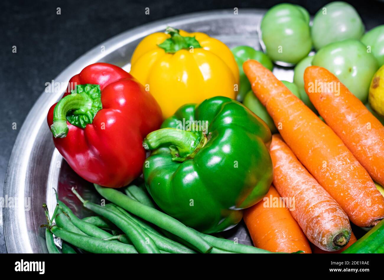 Selektive Konzentration von grünem Paprika, grünen Bohnen, rotem Paprika, Karotten auf einem Edelstahlteller mit verschiedenen Gemüsesorten Stockfoto