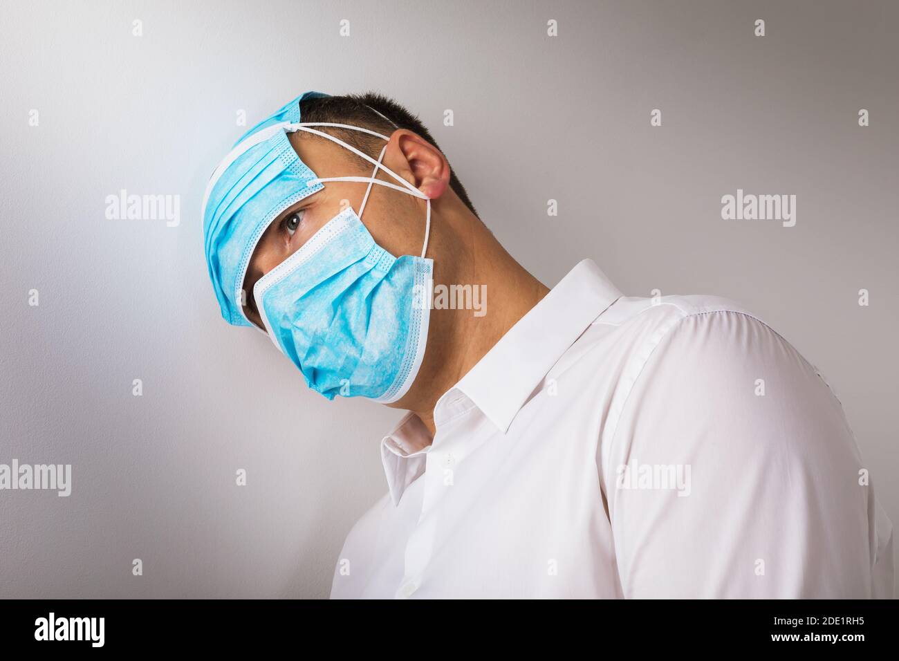 Der Mann in medizinischen Masken lehnte seinen Kopf gegen die Wand. Konzept zum Thema Depression aufgrund der Quarantäne durch das Coronavirus. Stockfoto