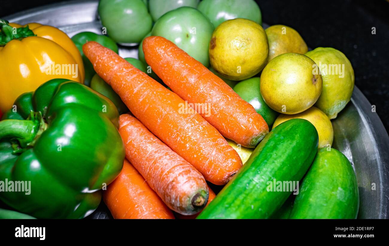 Selektive Konzentration von Karotten und Zitronen auf einem Edelstahlteller mit verschiedenen Gemüsesorten Stockfoto