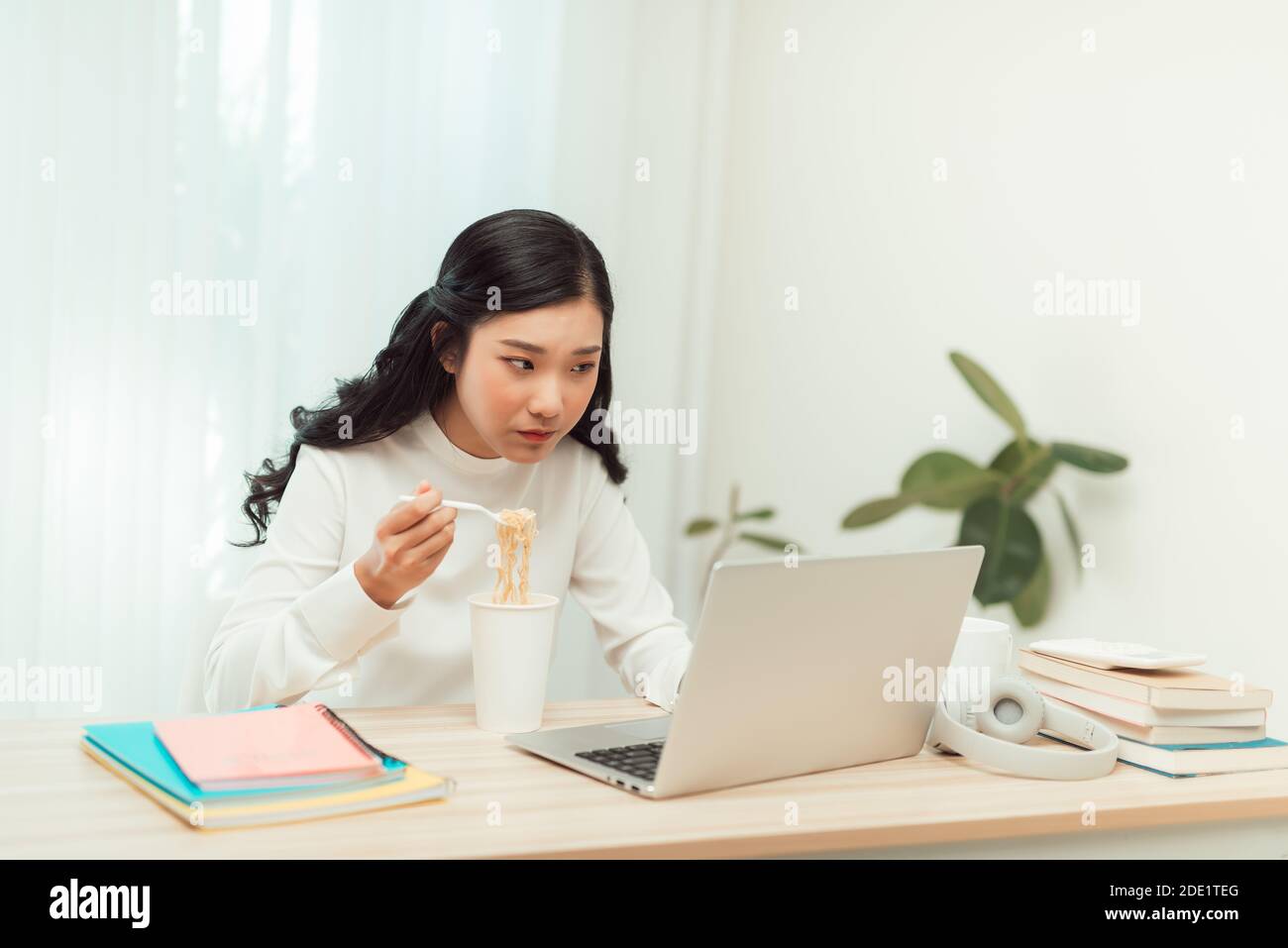 Asien freiberufliche Geschäftsfrau essen Instant Nudeln während der Arbeit an Laptop im Wohnzimmer im Heimbüro Stockfoto