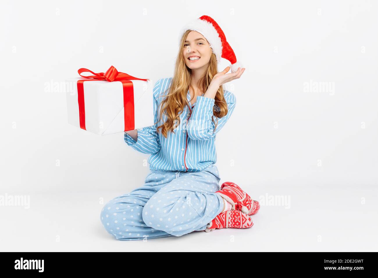 Weihnachtsmorgen. Happy schöne junge Mädchen, in Weihnachten Pyjamas und Weihnachtsmütze, öffnet Weihnachtsgeschenk, auf weißem Hintergrund Stockfoto