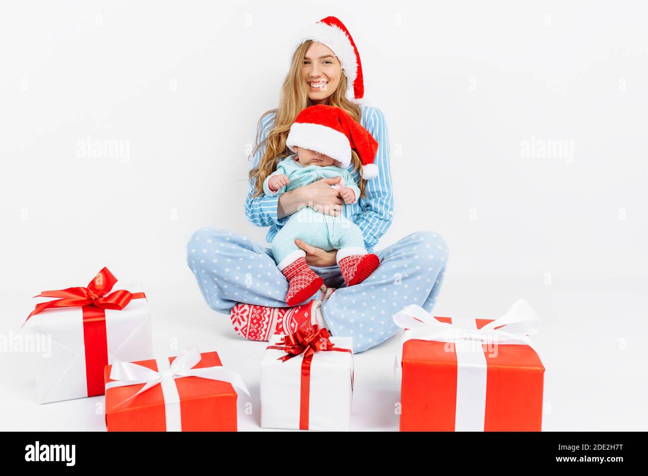 Eine junge Mutter, am Weihnachtstag gibt ein Geschenk an ein neugeborenes Kind, ein Mädchen hält ein Baby in den Armen mit einem Weihnachtsgeschenk, Weihnachtsmorgen in der Familie Stockfoto