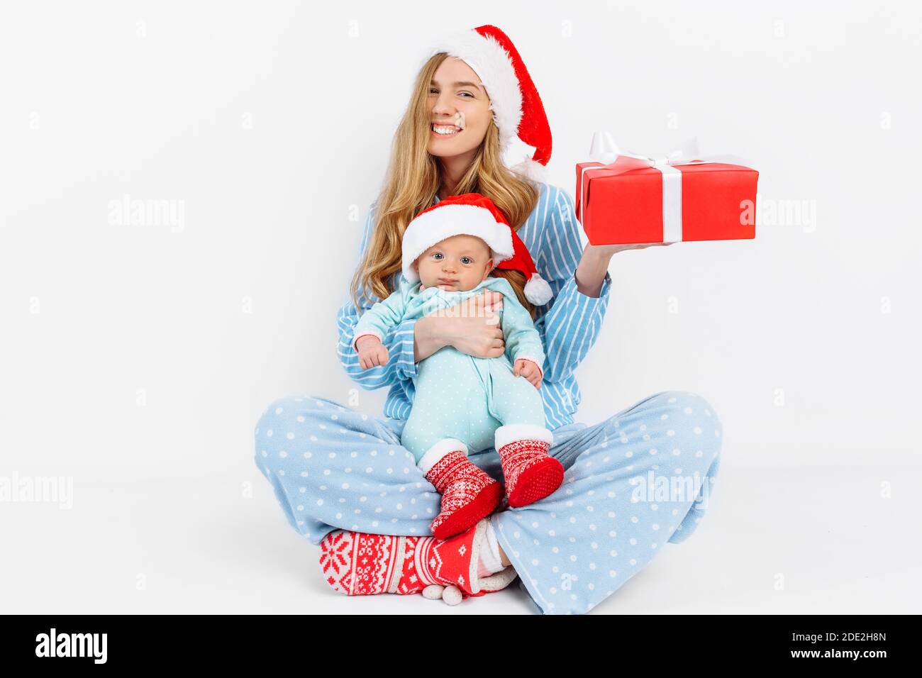 Eine junge Mutter, am Weihnachtstag gibt ein Geschenk an ein neugeborenes Kind, ein Mädchen hält ein Baby in den Armen mit einem Weihnachtsgeschenk, Weihnachtsmorgen in der Familie Stockfoto