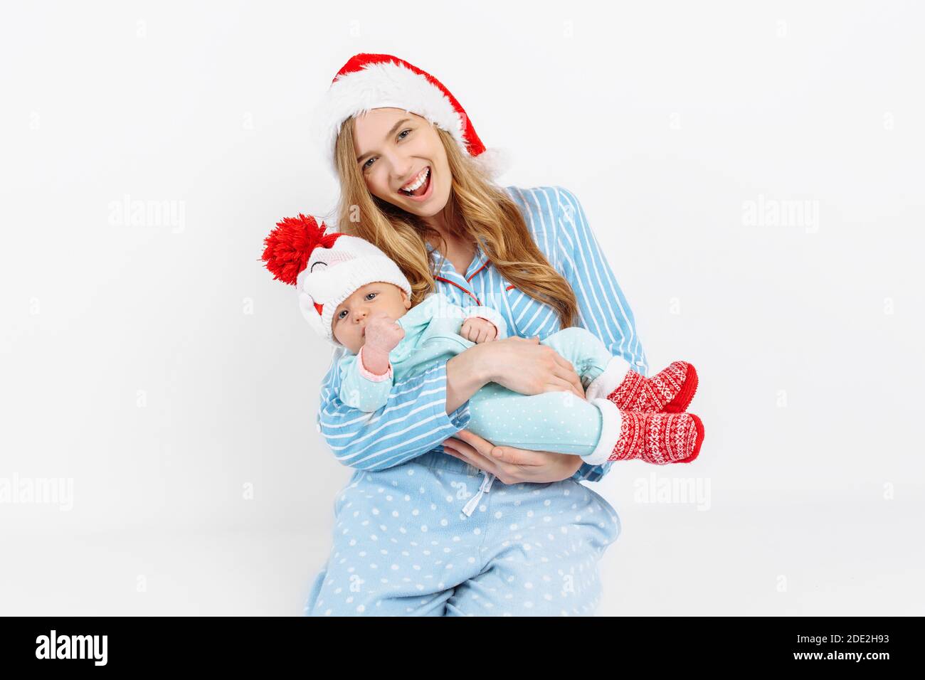 Eine junge Mutter, am Weihnachtstag gibt ein Geschenk an ein neugeborenes Kind, ein Mädchen hält ein Baby in den Armen in einem Weihnachtshut, Weihnachtsmorgen in der Familie, Stockfoto