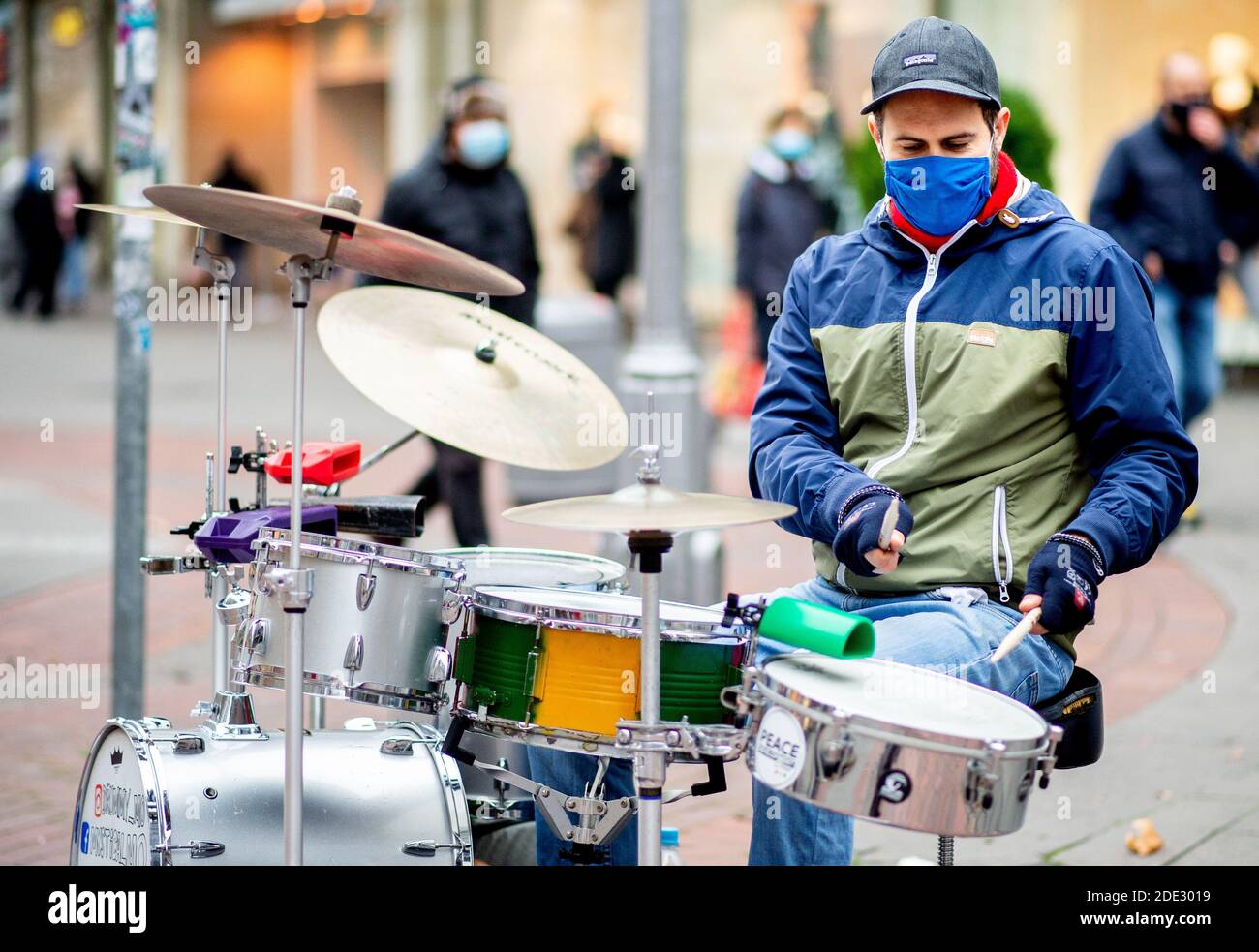 Hannover, Deutschland. November 2020. Der Musiker Moritz Dortmund spielt,  bekleidet mit einem Mundnasendeckel, auf seinen Trommeln in der Innenstadt.  Um große Menschenmengen zu vermeiden, hat er ein Schild vor seinem  Schlagzeug aufgestellt,