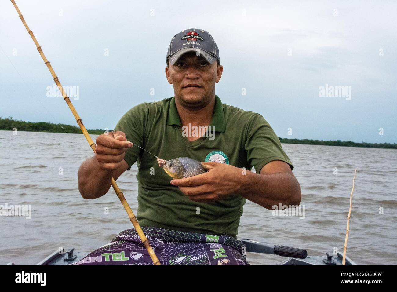 Ein brasilianischer Angler hat einen Gelben Bauch Piranha mit seinem Stock, als Angelrute und ein Stück Draht mit einem Haken in seinem Boot verwendet. Für Stockfoto