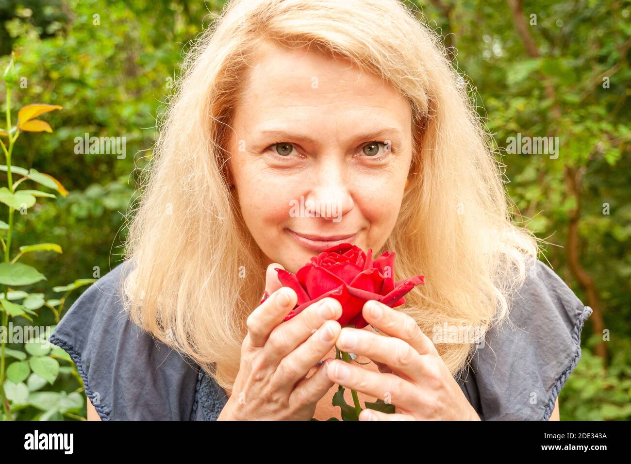 Blonde Frau mit einer roten Rose im Garten. Stockfoto