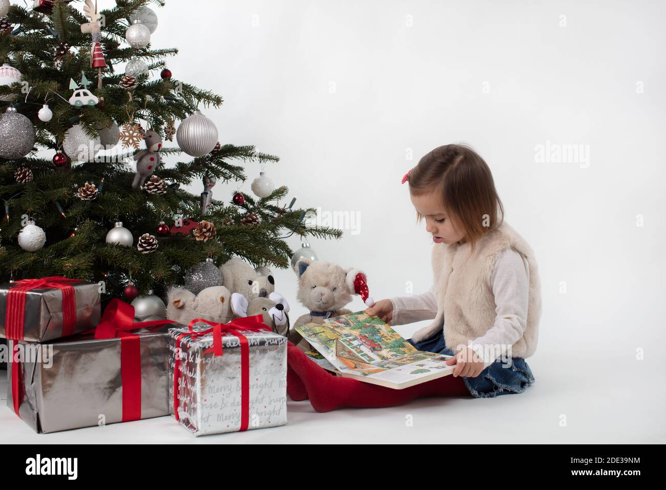 Ein Kleinkind Mädchen lesen Weihnachtsbuch zu ihrem weichen Spielzeug Freunde unter dem Weihnachtsbaum Stockfoto