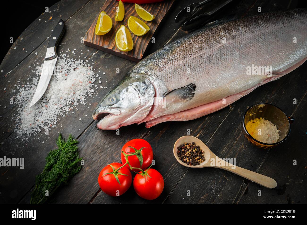 Großer frischer Lachs mit Zutaten zum Kochen auf Holzgrund Stockfoto