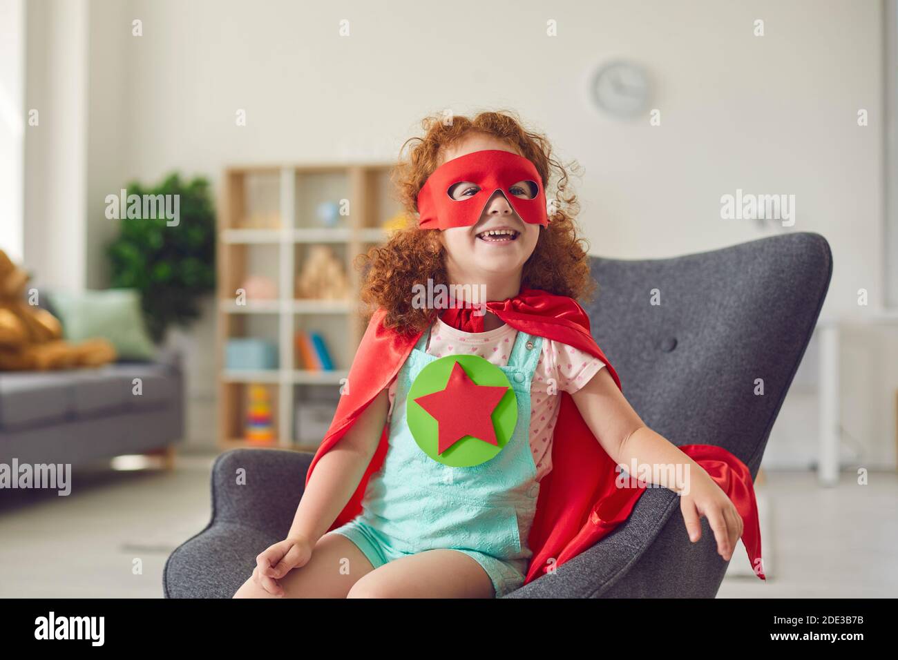 Portrait von Lachen glücklich rothaarige Mädchen in Kostüm von Superhelden-Star sitzt auf dem Sessel und lächelt Stockfoto Portrait von Lachen glücklich rothaarige Mädchen in Kostüm von Superhelden-Star sitzt auf dem Sessel und lächelt Stockfoto