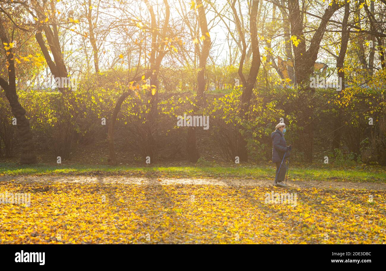 Aktive ältere Frau in Maske macht nordic Walk Übung in Der Park im Herbst warmen Tag Stockfoto