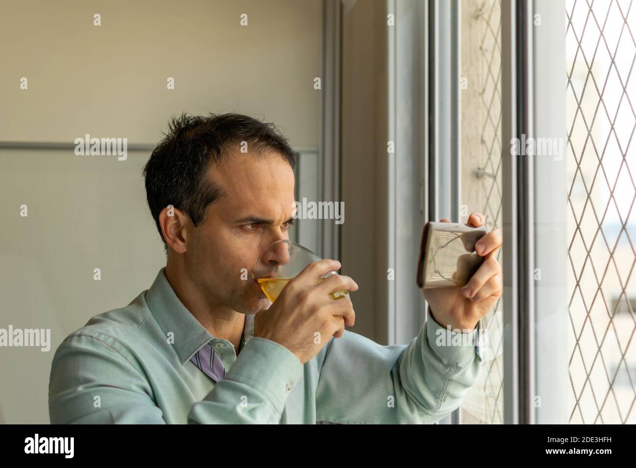 Reifer Mann (44 Jahre alt) trinkt Whiskey und schaut sich Videos auf seinem Smartphone an. Stockfoto