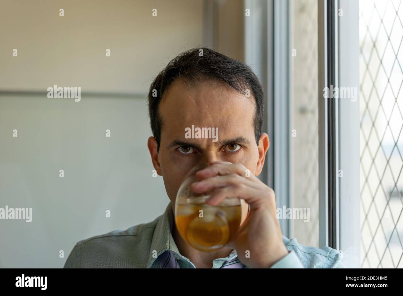 Nahaufnahme eines reifen Mannes (44 Jahre alt), der Whisky trinkt und auf die Kamera starrt. Stockfoto
