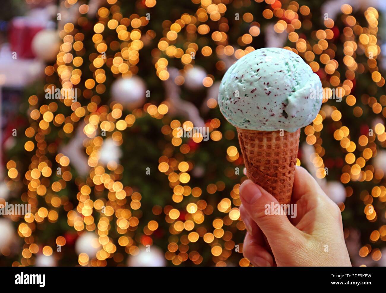 Nahaufnahme ein Scoop von Mint Chocolate Chip Ice Cream Cone In der Hand mit glitzernden Weihnachtsbaum Bokeh im Hintergrund Stockfoto