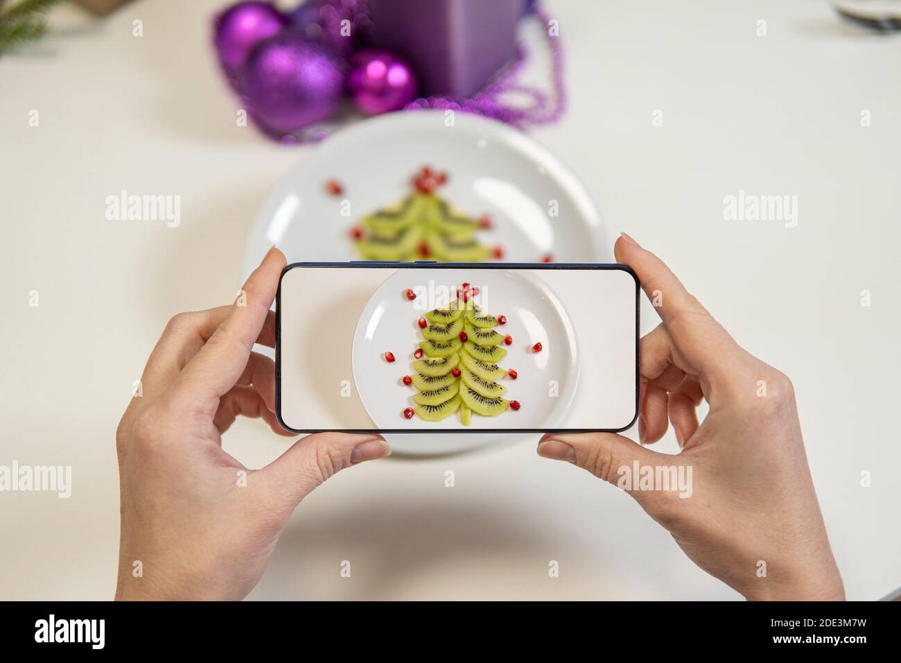 Mädchen Hand macht Bilder von Weihnachtstisch. weihnachten Tischdekoration. Kiwi und Granatapfel in Form eines weihnachtsbaums auf einem Teller. High qu Stockfoto