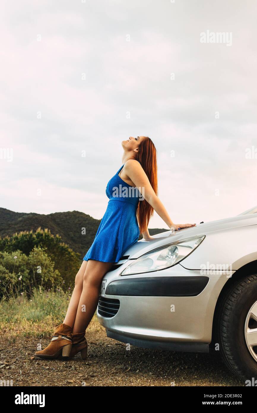 Junge Frau, die auf EINEM Auto steht und alleine aufschaut In Der Natur Stockfoto