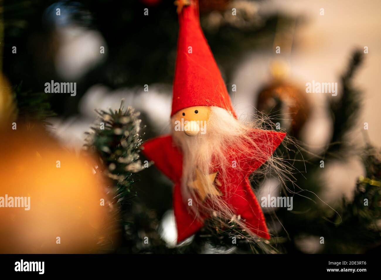 Thema „Neujahr“. Nahaufnahme. Weihnachtsspielzeug von weihnachtsmann in roten Gewändern hängt auf grünen Nadeln eines künstlichen Weihnachtsbaums. Stockfoto