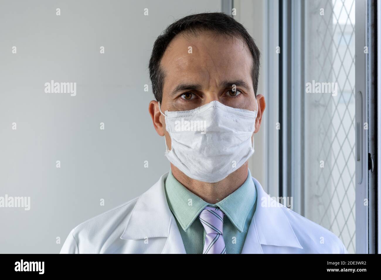 44 Jahre alter Arzt mit Maske, weißem Mantel und Krawatte. Stockfoto