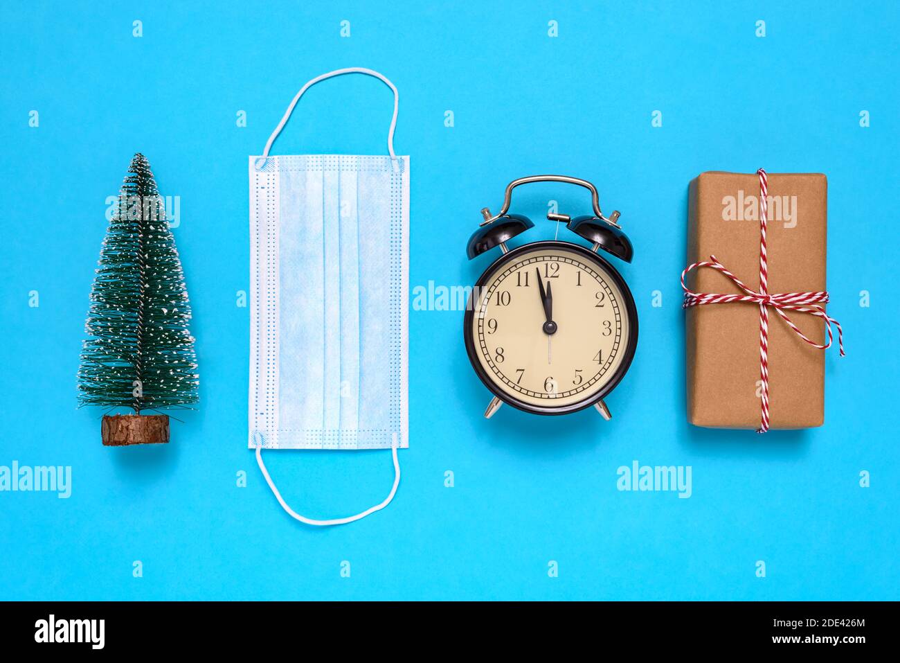 Kleiner Weihnachtsbaum, Geschenkbox, Wecker, Schutzmaske auf blauem Hintergrund. Stockfoto