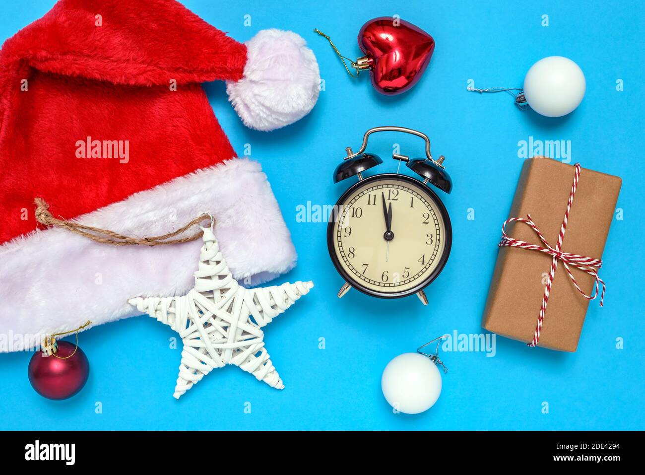 Weihnachtsmann Hut, Wecker, Geschenkbox und dekorative Weihnachtsschmuck auf blauem Hintergrund. Das Konzept der Feier des neuen Jahres und Weihnachten. Stockfoto