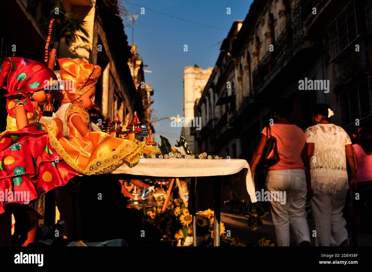 Zwei religiöse Puppen, eine in gelb und die andere in rot gekleidet, auf einem Tisch mit religiösen Dingen und Blumen, Frauen, die die Straße eines alten Stockfoto