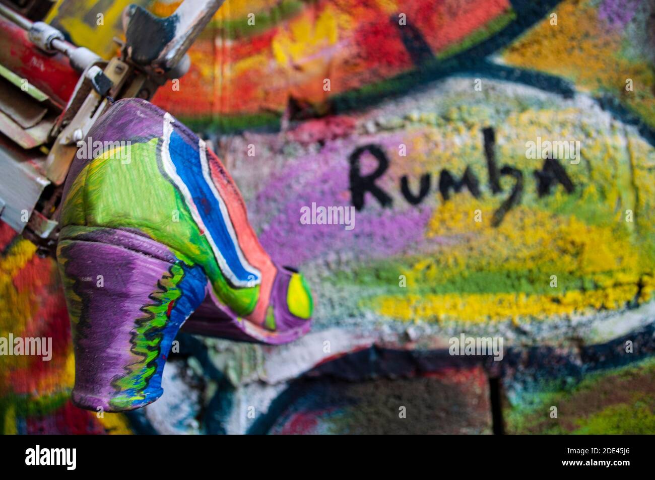 Flamenco-Tanzschuh in verschiedenen Farben gemalt, hängt von einer alten Schreibmaschine an einer Wand von vielen Farben und mit dem Wort Rumba darauf geschrieben, moderne ein Stockfoto
