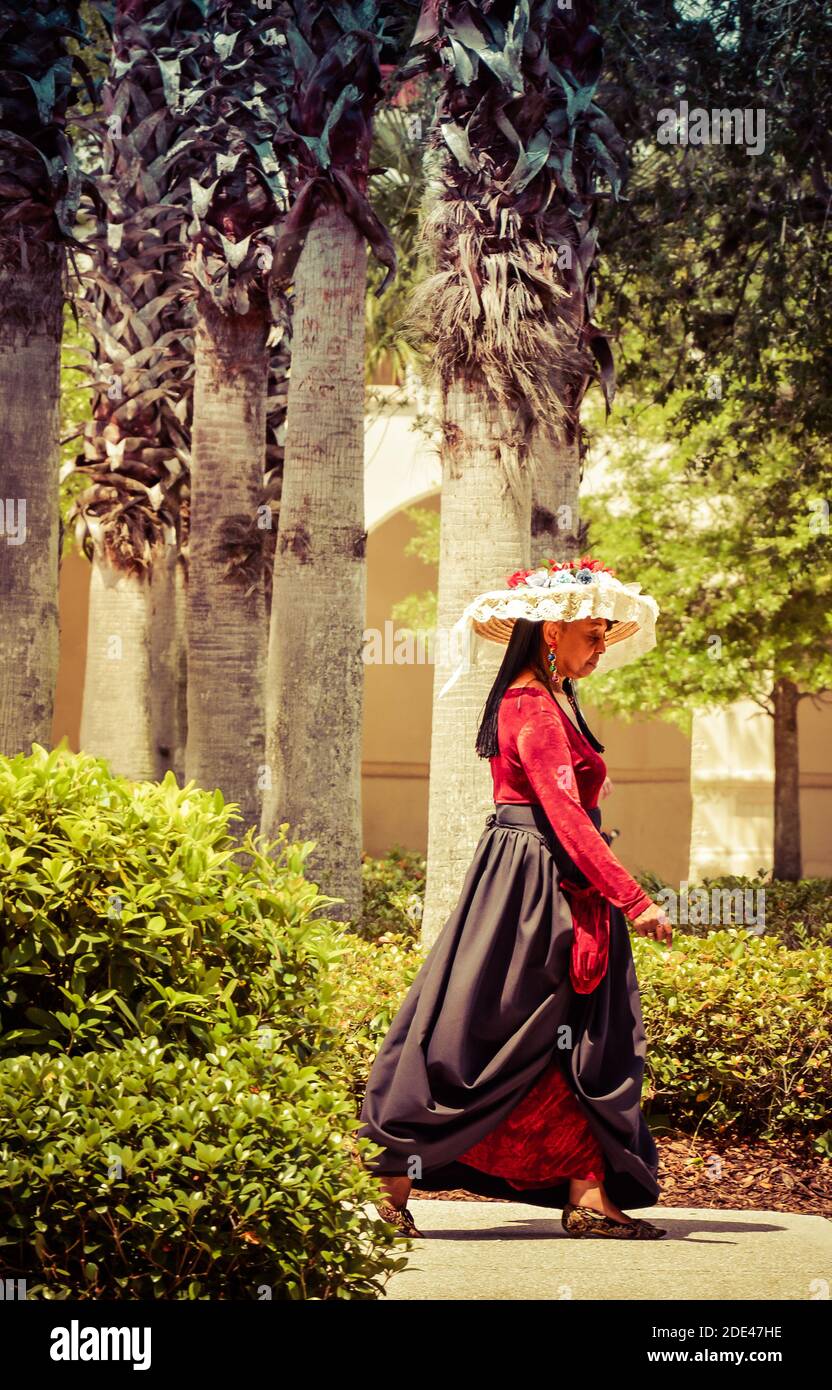 Ein schöner kultureller Blitz einer Frau mit Farbe trägt Festlicher spanischer Sommerhut mit Spitze und Blumen und rot Samtkleid zu Fuß in der Innenstadt unter Stockfoto