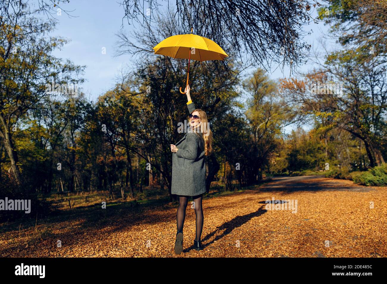 Rückansicht, ein stilvolles Mädchen in einem Mantel und mit einem gelben Regenschirm, Spaziergang durch den Park mit gelben Blättern, genießen Sie die herbstliche Wärme. Herbstzeit Stockfoto