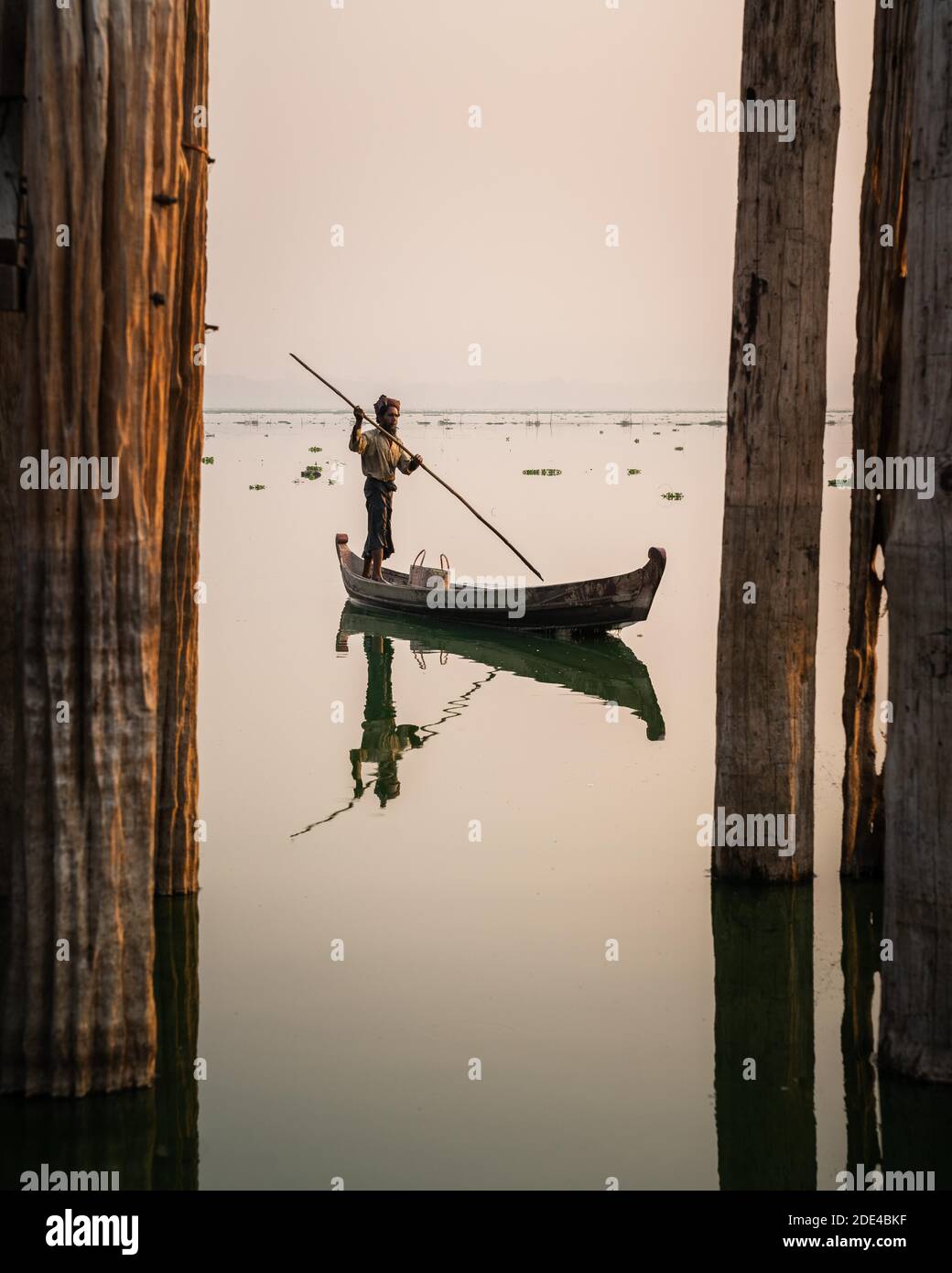 Fischer steht mit Boot auf Taung Tha man Lake für Sonnenaufgang zwischen den Pfosten der U-Bein-Brücke, Reflexion im Wasser, Thaung Tha man Lake Stockfoto