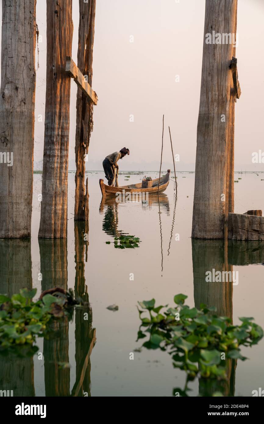 Fischer steht mit Boot auf Taung Tha man Lake für Sonnenaufgang zwischen den Pfosten der U-Bein-Brücke, Reflexion im Wasser, Thaung Tha man Lake Stockfoto